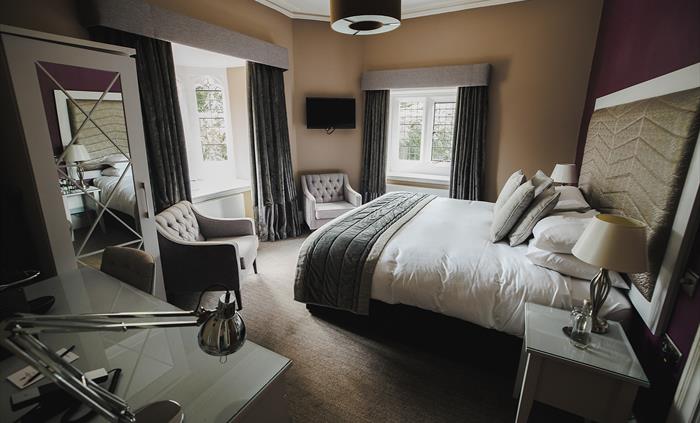 A hotel bedroom with arm chairs at foot of the bed and a tv on the wall.